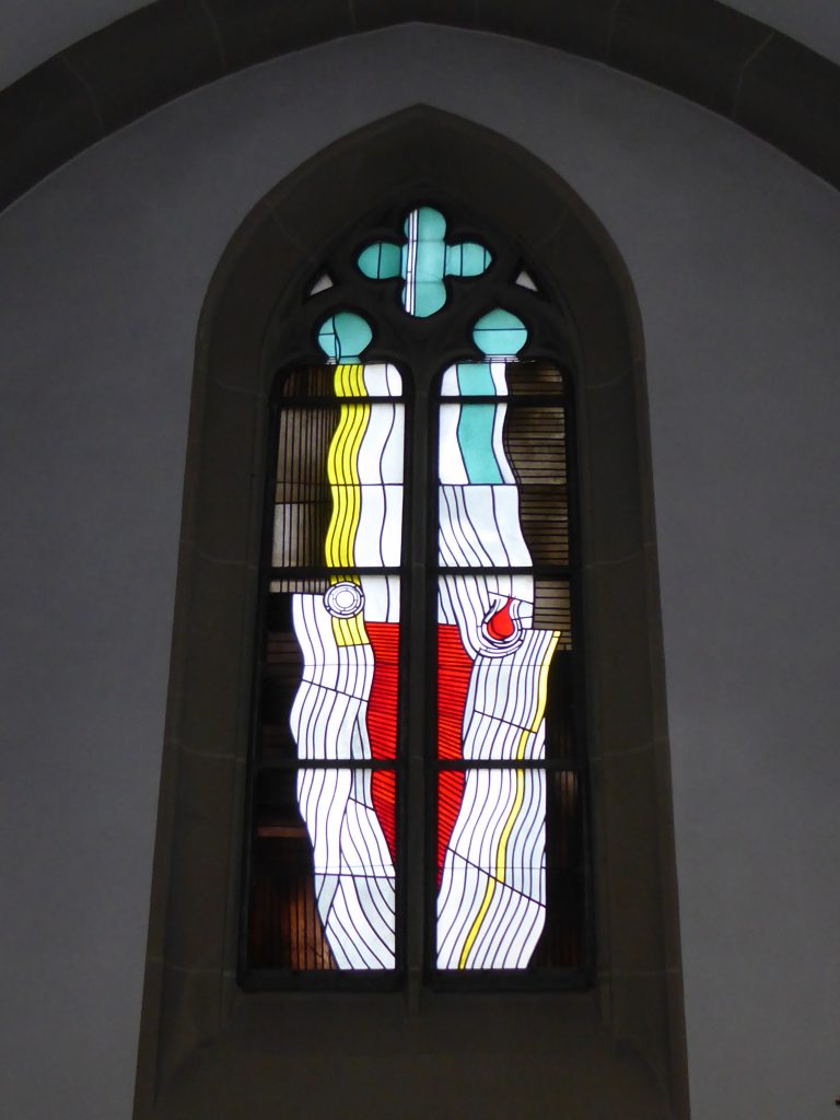 Seitenschiff – Fronleichnam und Herz-Jesu-Fest: Links wird Fronleichnam durch das Brot symbolisiert. Das rote Herz rechts steht für das Herz-Jesu-Fest, an dem das Patrozinium (Hochfest, das den Heiligen feiert, dem die Kirche geweiht ist) der Kirche begangen wird.